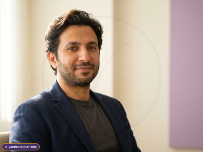 رجل عربي بشعر علوي كامل الطول ولحية مشذبة يبتسم بثقة في ردهة مركز يور هير، نموذج لنتيجة زراعة الشعر بدون حلاقة بتقنية FUE